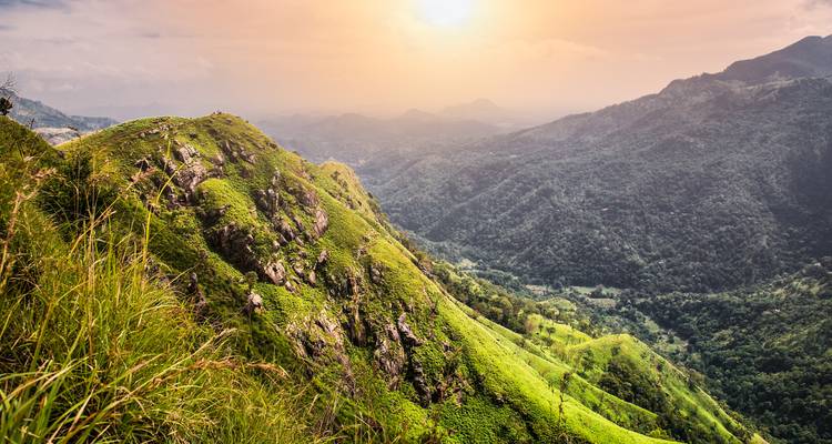 La lumière du coucher de soleil baigne les crêtes des montagnes d'un vert éclatant surplombant une vaste vallée brumeuse.