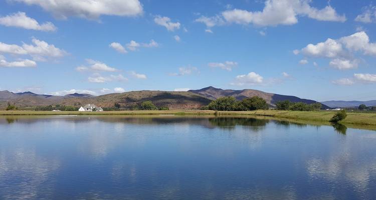 A lake reflecting a hilly landscape under a blue sky with clouds.