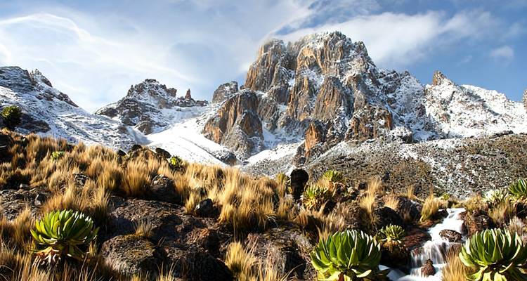 Schnebedeckte zerklüftete Gipfel des Mount Kenya erheben sich über goldene alpine Vegetation und einen kleinen Wasserfall