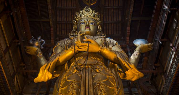 Una majestuosa estatua de Buda dorado se alza imponente dentro de un salón de oración de madera oscura.