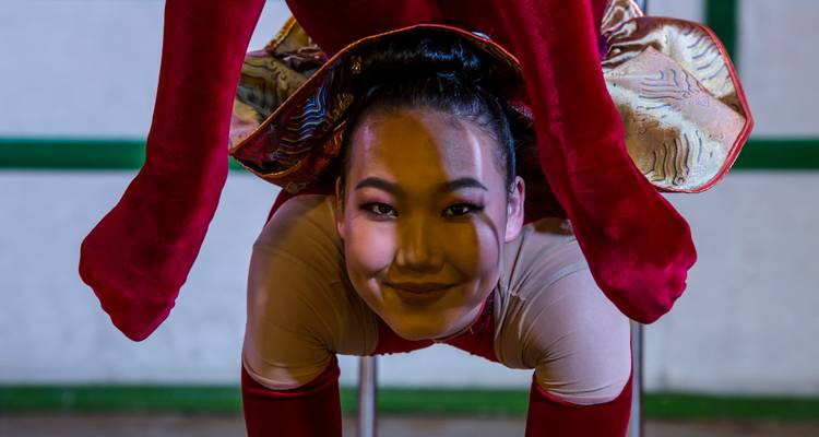 Contorsionista sonriente en traje rojo posa en un impresionante arco hacia atrás en el escenario.