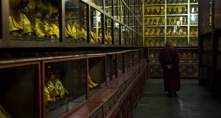 Un monje solitario camina por un pasillo oscuro bordeado de filas de estatuas doradas de Buda.