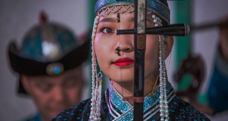 Primer plano de un artista mongol con atuendo tradicional sosteniendo una espada durante un espectáculo cultural.