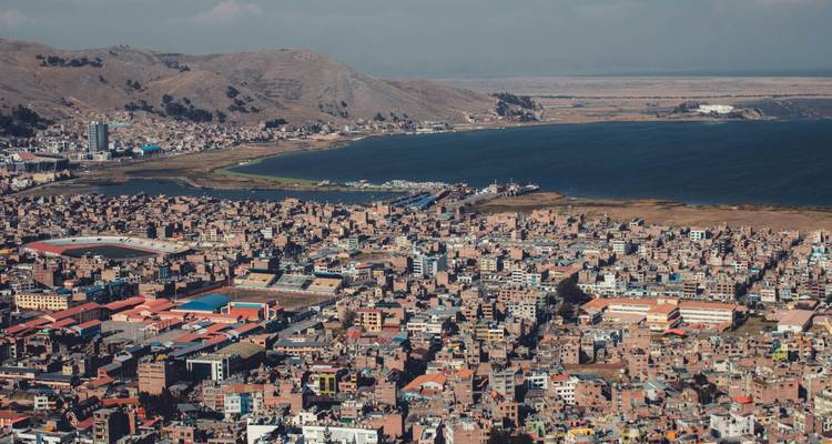 Panorama aérien de la ville de Puno s'étendant le long de la baie du lac Titicaca avec des collines arides s'élevant derrière le rivage.