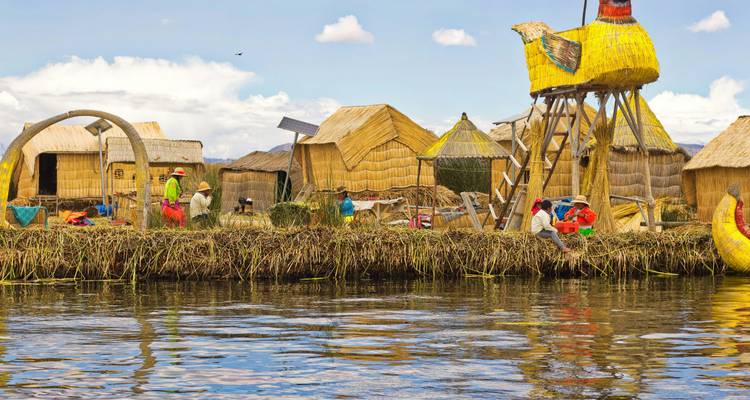 Los lugareños con ropa tradicional colorida trabajan y conversan en una isla flotante de juncos con chozas de paja que se reflejan en el agua.