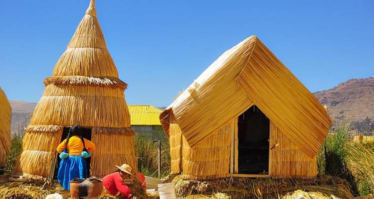 Locals in colourful skirts work outside cone-shaped reed huts beneath a clear blue Andean sky.