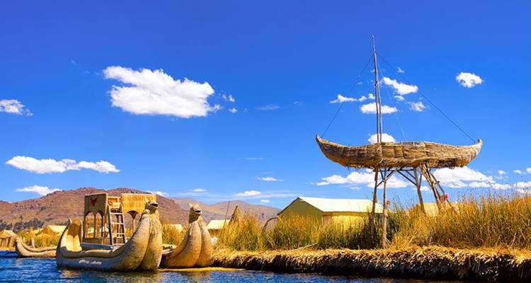 Graceful crescent-shaped reed boats and a raised reed catamaran float near golden islands under a vivid blue sky.