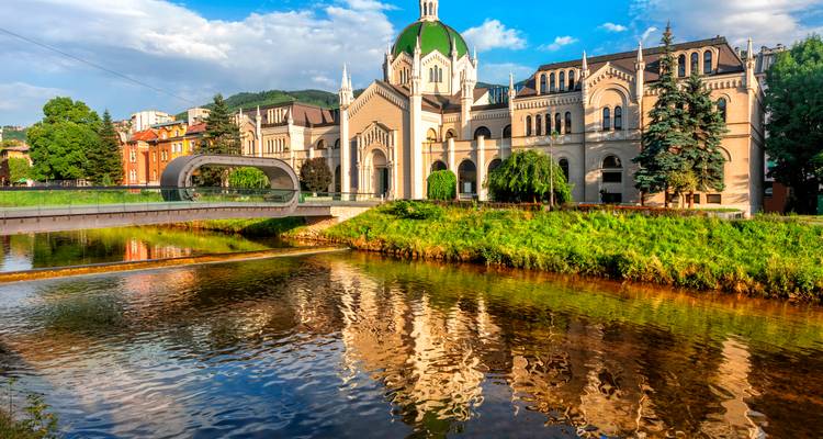 Historic building with green dome by a river under blue sky.