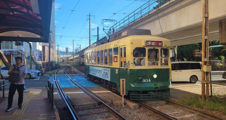 Een vintage groene tram wacht op een zonnig station onder een viaduct in de regio Hiroshima.