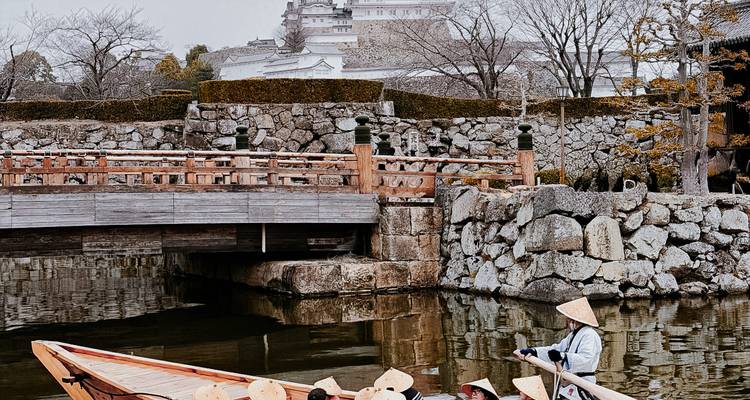 Bootsman in strohoeden glijden met een houten bootje onder de stenen muren en brug van Himeji Castle door.