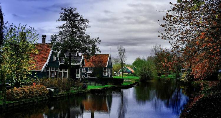 Escena rural con casas a lo largo de un canal bordeado de árboles.