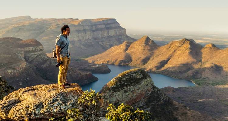 Mann, der auf einer Klippe steht und auf eine Bergkette blickt.