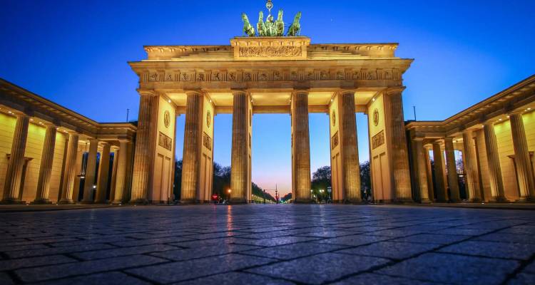 Beleuchtetes Brandenburger Tor aus niedriger Perspektive vor tiefblauem Himmel.