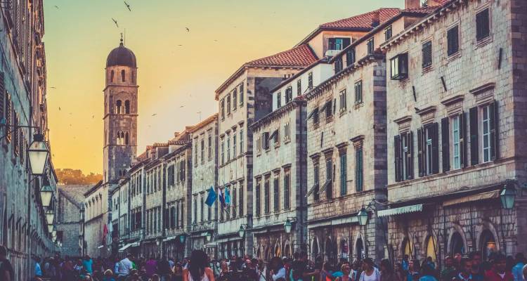 Menigten flaneren tijdens het gouden uur langs de Stradun van Dubrovnik met de beltorre die gloeit.