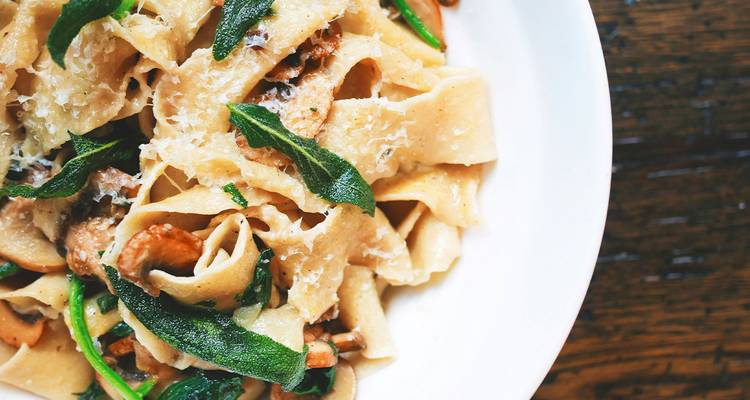 Nahaufnahme von frischer Tagliatelle-Pasta mit Salbei und Pilzen auf einem weißen Teller