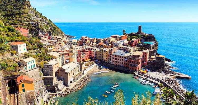Las casas coloridas de Vernazza y su pequeño puerto vistos desde una altura bajo cielos azules