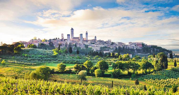 Mittelalterliche Türme von San Gimignano erheben sich über sanft hügelige toskanische Weinberge unter einem dramatischen Himmel.