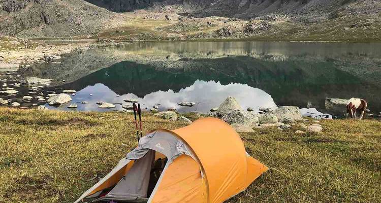 Een tent bij een reflecterend meer met bergen op de achtergrond.