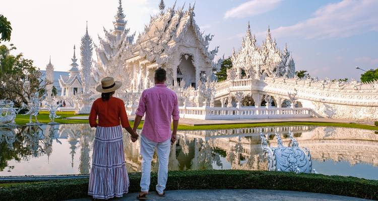 Pareja admirando un templo blanco ornamentado con un estanque.