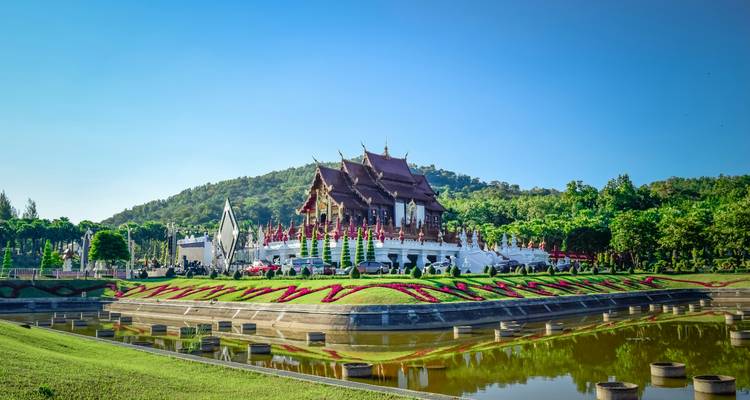 Un edificio tradicional tailandés con jardines y montañas al fondo.