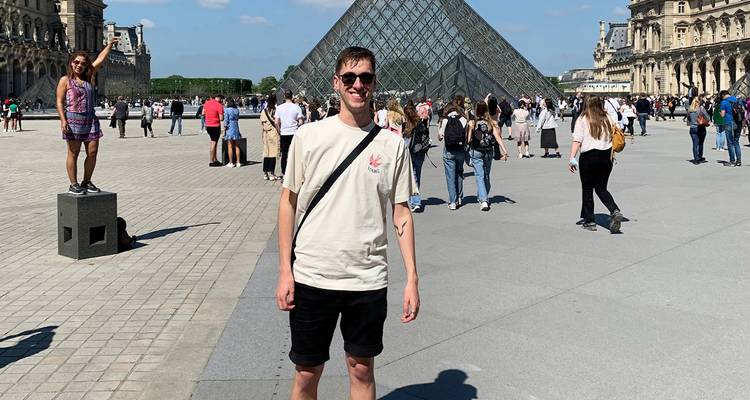 Menschen vor dem Louvre mit der prominent sichtbaren Glaspyramide.