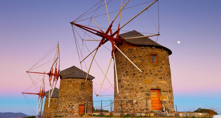 Sunset view of traditional windmills with a pink sky in Mykonos.