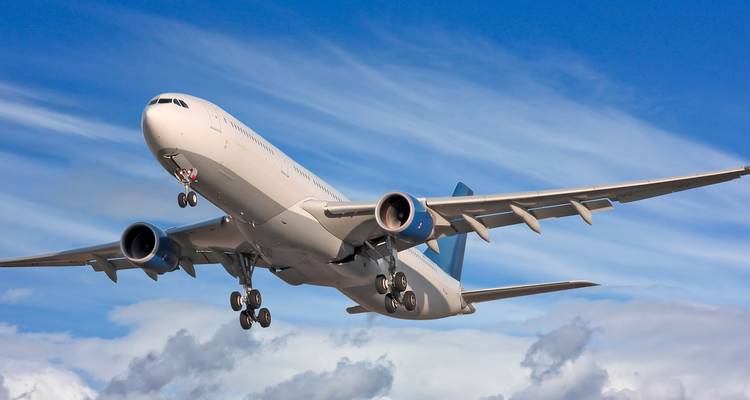 Commercial airliner captured mid-flight against a vivid blue sky with streaked clouds.