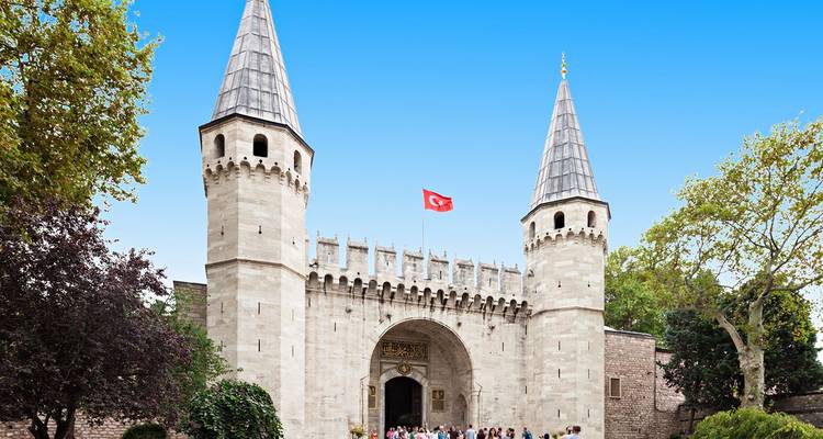 Stenen poort met twee puntige torens en Turkse vlag die de ingang van het Topkapi-paleis aangeeft terwijl toeristen buiten samenkomen.
