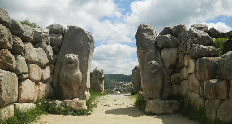 Antikes Steintor, das von zwei geschnitzten Löwenstatuen flankiert wird, unter einem teilweise bewölkten Himmel.