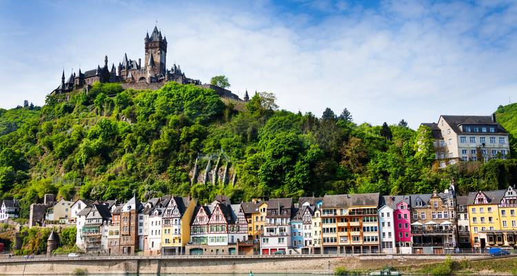 Vue panoramique des maisons riveraines colorées de Cochem couronnées par le château perché sur la colline au milieu de la verdure luxuriante.