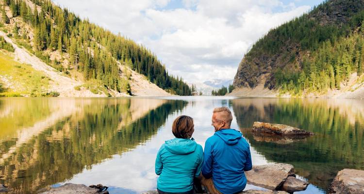 Pareja sentada junto a un lago tranquilo con colinas boscosas.