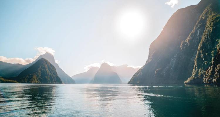 Mirror-calm water reflects soaring peaks and morning sun in the dramatic fjord of Milford Sound.