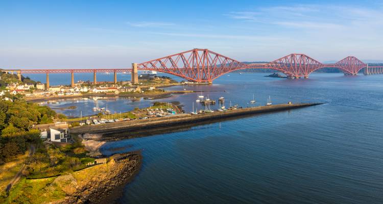 Die ikonische rote Forth Bridge erstreckt sich über die blaue Firth of Forth und wird an einem klaren Tag von oben betrachtet.