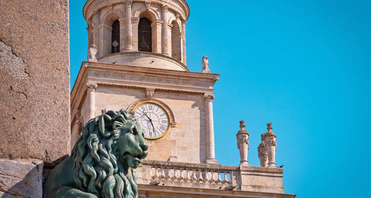 Tour de l'horloge s'élevant derrière une statue de lion en bronze sous un ciel bleu éclatant.