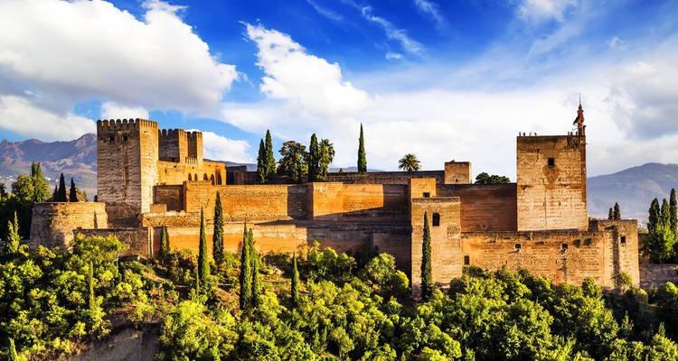 Le complexe forteresse de l'Alhambra situé au-dessus de végétation luxuriante avec des nuages dramatiques.