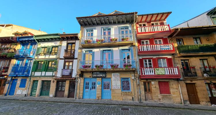 Rangée de maisons de ville en bois aux couleurs vives avec des balcons sur une rue pavée.