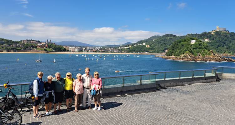 Groupe de voyageurs posant sur une promenade en bord de mer avec une baie panoramique en arrière-plan.