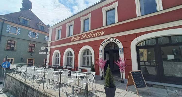 Café Rathaus mit roter Fassade und Außensitzbereich auf einer ruhigen Straße.