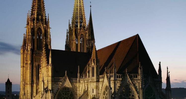 Der Regensburger Dom silhouettiert in der Dämmerung mit subtiler warmer Beleuchtung auf den Spitzen.