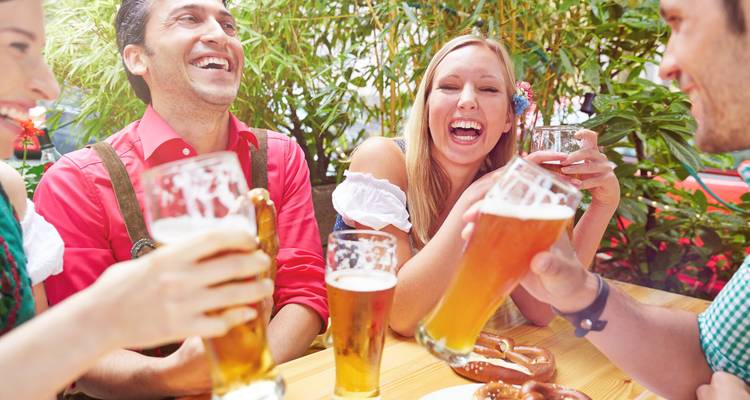 Freunde, die an einem Außentisch große Biergläser halten und anstoßen und lachen.