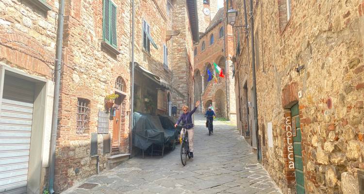 Los ciclistas recorren una estrecha calle empedrada entre edificios de ladrillo rústicos.