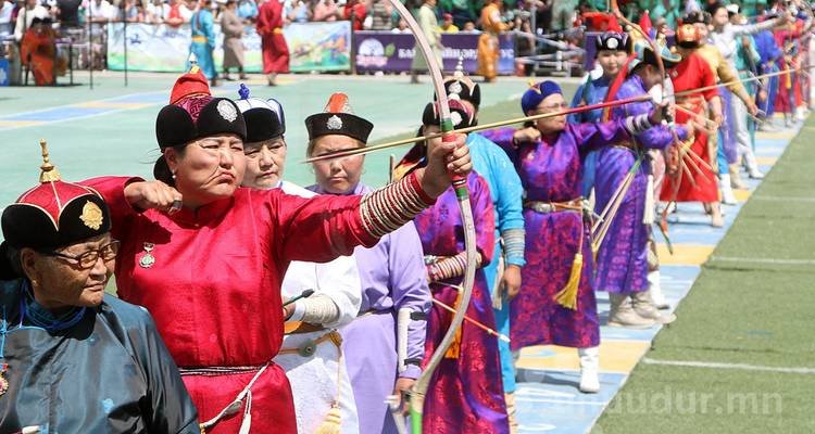 Une longue rangée d'archers en costumes traditionnels éclatants bandent leurs arcs sur un terrain de sport ; un filigrane est visible dans le coin.