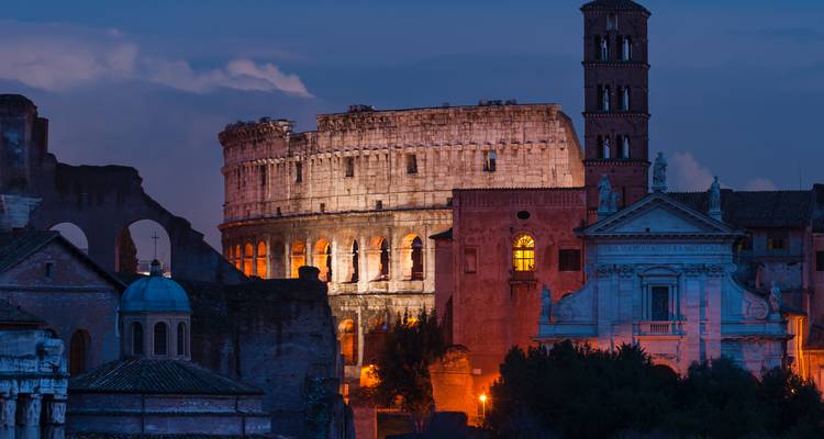 Le Colisée de Rome illuminé au crépuscule, entouré de ruines antiques dans un profond crépuscule bleu.