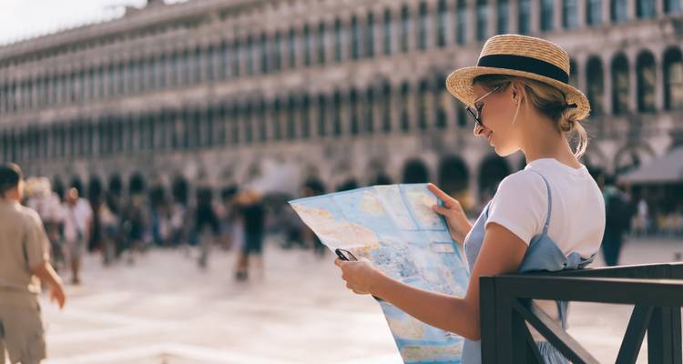 Jeune femme portant un chapeau de paille étudie une carte sur la Piazza San Marco ensoleillée de Venise.