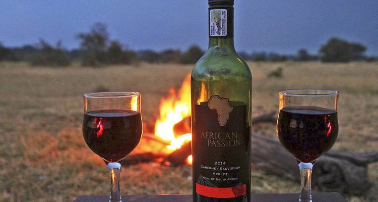Weinaufbau mit Gläsern und Flasche an einem Lagerfeuer unter einem dunkler werdenden Himmel.