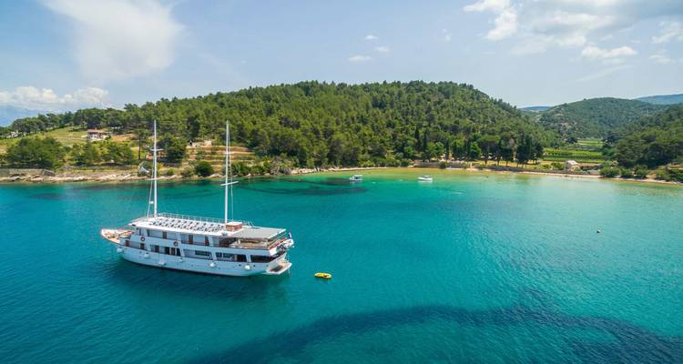 Eine Yacht vor Anker in türkisfarbenen Gewässern nahe einer bewaldeten Insel.