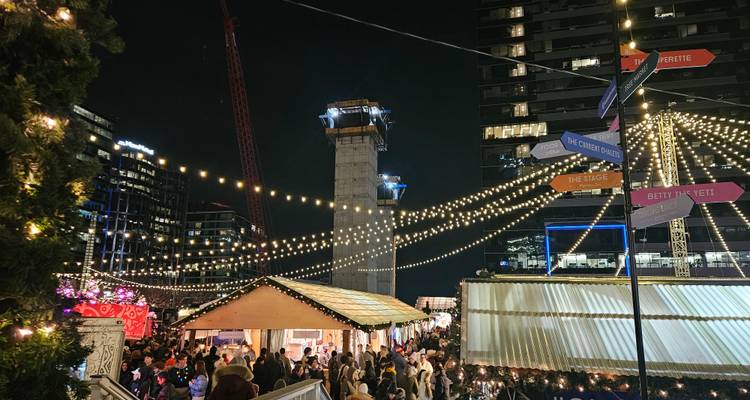 Bustling nighttime Christmas market with strings of fairy lights, food stalls and crowds of visitors.