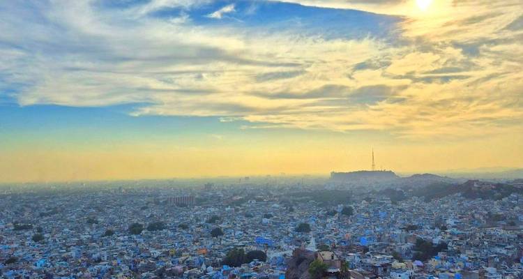 Expansive sunset view over the blue houses of Jodhpur with distant hills and golden sky.