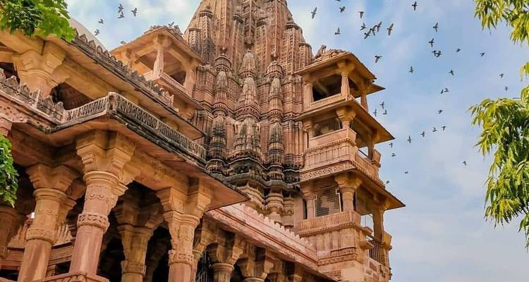 Intricately carved pink sandstone temple with birds circling in the morning sky.