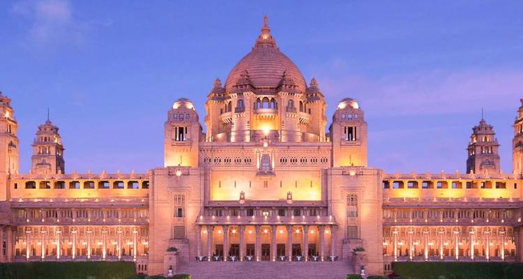 Umaid Bhawan Palace illuminated in warm evening lights against a violet sky.